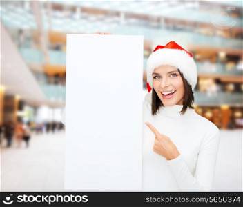 winter holidays, christmas, advertising and people concept - smiling young woman in santa helper hat with white blank billboard over shopping center background