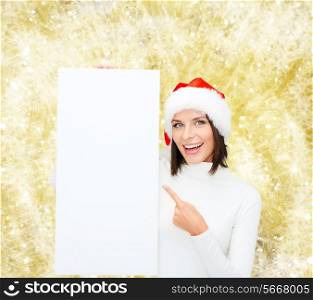 winter holidays, christmas, advertising and people concept - smiling young woman in santa helper hat with white blank billboard over yellow lights background