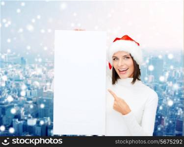winter holidays, christmas, advertising and people concept - smiling young woman in santa helper hat with white blank billboard over snowy city background