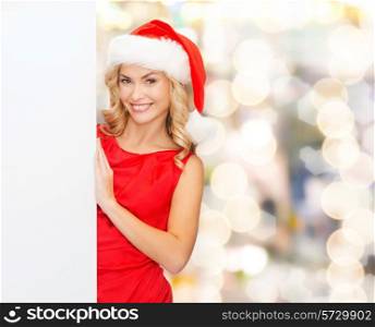 winter holidays, christmas, advertising and people concept - smiling young woman in santa helper hat with white blank billboard over lights background