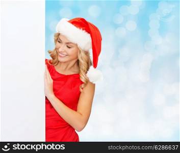 winter holidays, christmas, advertising and people concept - smiling young woman in santa helper hat with white blank billboard over blue lights background
