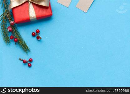 winter holidays, christmas and celebration concept - red gift box and fir tree branches with berries on blue background. christmas gift and fir branches with berries