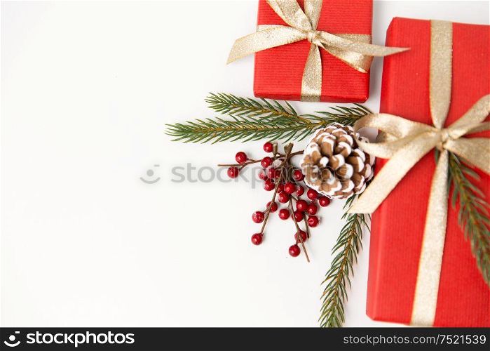 winter holidays, christmas and celebration concept - red gift boxes and fir tree branches with pine cones on white background. christmas gifts and fir branches with pine cones