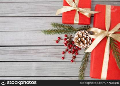 winter holidays, christmas and celebration concept - red gift boxes and fir tree branches with pine cones on wooden boards background. christmas gifts and fir branches with pine cones