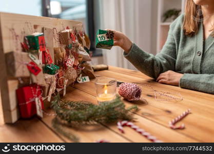 winter holidays, christmas and hobby concept - hands hanging gift with tag to handmade advent calendar at home. hands making christmas advent calendar at home