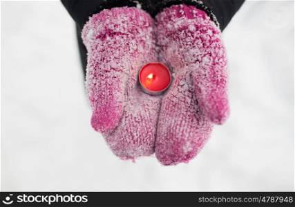winter holidays, christmas and people concept - close up of hands in mittens holding burning tea candle outdoors