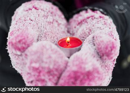 winter holidays, christmas and people concept - close up of hands in mittens holding burning tea candle outdoors