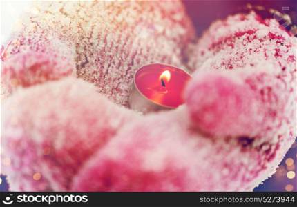 winter holidays, christmas and people concept - close up of hands in mittens holding burning tea candle outdoors. close up of hands in winter mittens holding candle