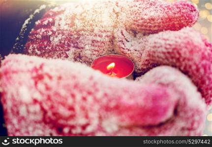 winter holidays, christmas and people concept - close up of hands in mittens holding burning tea candle outdoors. close up of hands in winter mittens holding candle