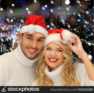 winter, holidays, christmas and people concept - smiiling couple in sweaters and santa helper hats over snowy night city background