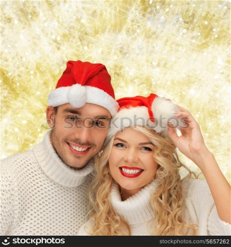 winter, holidays, christmas and people concept - smiling couple in sweaters and santa helper hats over yellow lights background