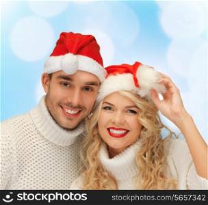 winter, holidays, christmas and people concept - smiling couple in sweaters and santa helper hats over blue lights background