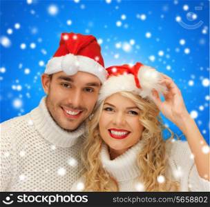 winter, holidays, christmas and people concept - smiling couple in sweaters and santa helper hats over blue snowy background