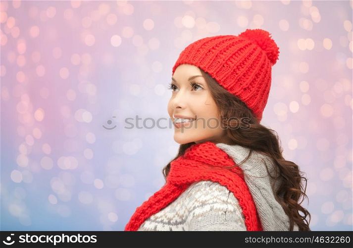 winter holidays, christmas and people concept - smiling young woman in red hat and scarf over rose quartz and serenity lights background
