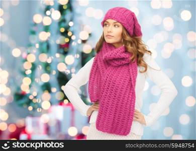 winter holidays, christmas and people concept - young woman in hat and scarf over christmas tree lights background