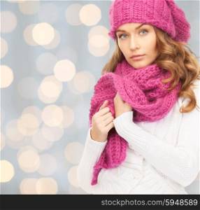 winter holidays, christmas and people concept - young woman in hat and scarf over lights background