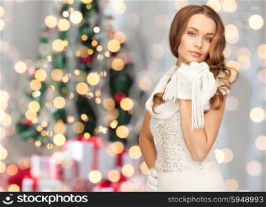 winter holidays, christmas and people concept - young woman in white cloves and scarf over christmas tree lights background
