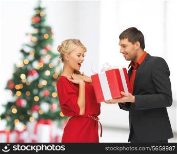 winter, holidays, christmas, celebration and people concept - smiling man and woman with present over living room with christmas tree background