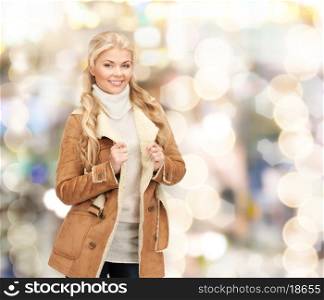 winter holidays, christmas, fashion and people concept - smiling young woman in winter clothes over lights background