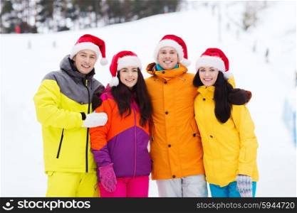 winter holidays, christmas, friendship and people concept - happy friends in santa hats and ski suits outdoors