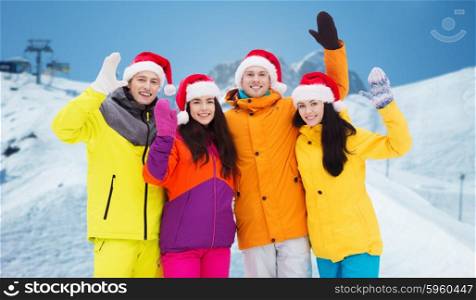 winter holidays, christmas, friendship and people concept - happy friends in santa hats and ski suits over downhill skiing and mountains background