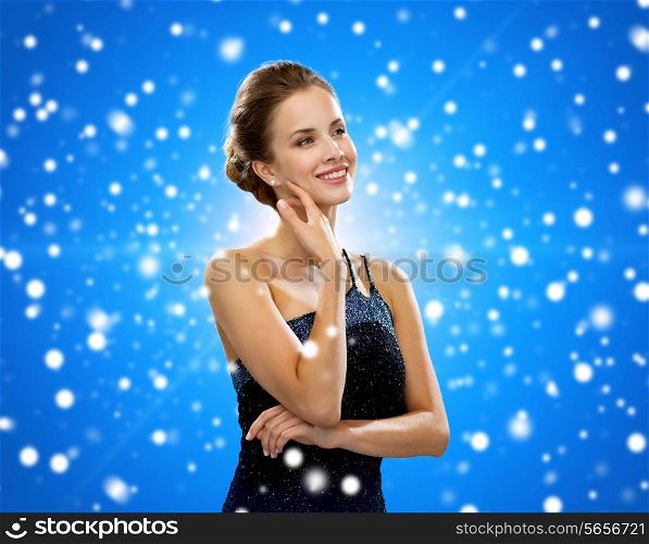 winter holidays, christmas, people and glamour concept - smiling woman in evening dress over black background over blue snowy background