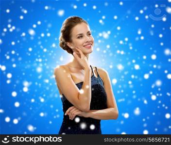 winter holidays, christmas, people and glamour concept - smiling woman in evening dress over black background over blue snowy background