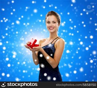 winter holidays, christmas, presents, luxury and happiness concept - smiling woman in dress holding red gift box over blue snowy background