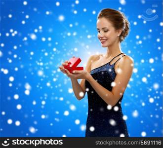 winter holidays, christmas, presents, luxury and people concept - smiling woman in dress holding red gift box over blue snowy background