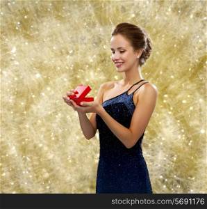 winter holidays, christmas, presents, luxury and people concept - smiling woman in dress holding red gift box over yellow lights background
