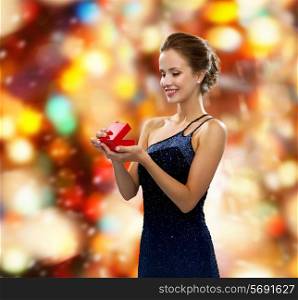 winter holidays, christmas, presents, luxury and people concept - smiling woman in dress holding red gift box over red lights background