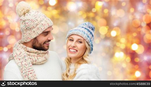 winter, holidays, couple, christmas and people concept - smiling man and woman in hats and scarf over lights background