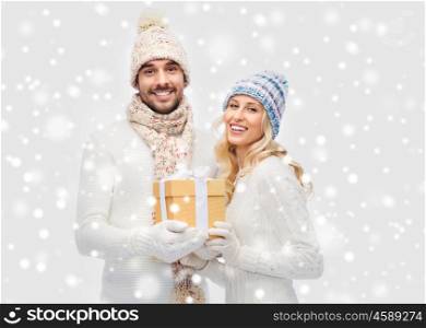 winter, holidays, couple, christmas and people concept - smiling man and woman in hats and scarf with gift box