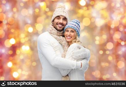 winter, holidays, couple, christmas and people concept - smiling man and woman in hats and scarf hugging over lights background