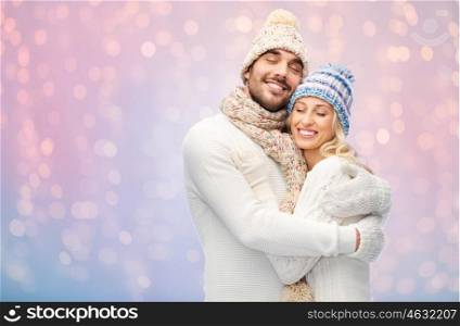 winter, holidays, couple, christmas and people concept - smiling man and woman in hats and scarf hugging over rose quartz and serenity lights background