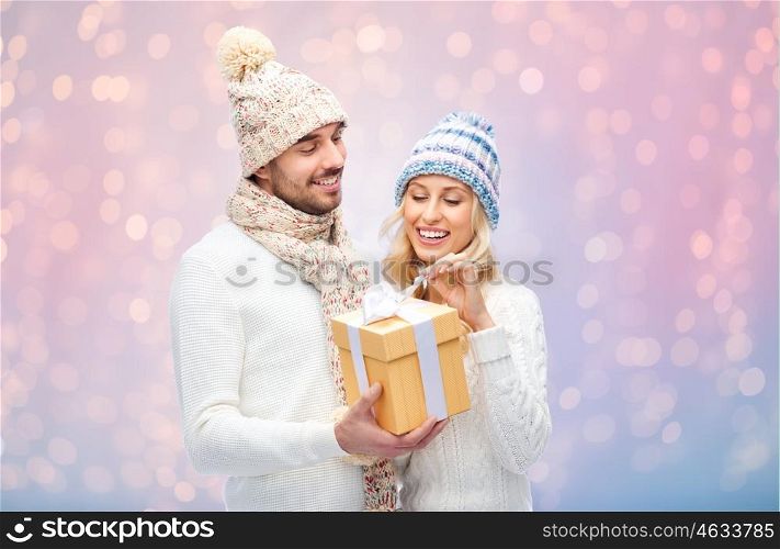 winter, holidays, couple, christmas and people concept - smiling man and woman in hats and scarf with gift box over rose quartz and serenity lights background