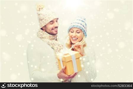 winter, holidays, couple, christmas and people concept - smiling man and woman in hats and scarf with gift box. smiling couple in winter clothes with gift box