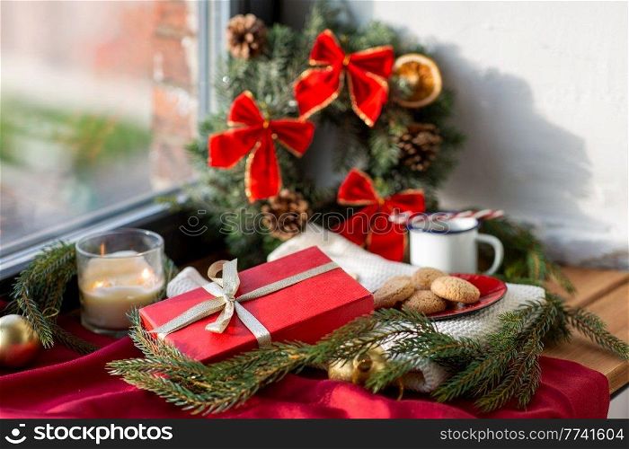 winter holidays, decoration and celebration concept - christmas gift, cookies, candle and fir branch on window sill at home. christmas gift, cookies, candle and fir branch
