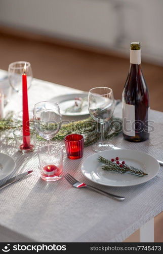 winter holidays, dinner party and celebration concept - christmas table serving with candles, crockery and wine at home. christmas dinner party table serving at home