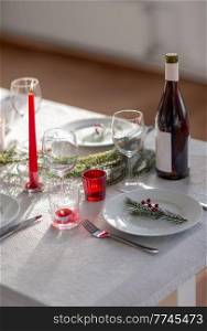 winter holidays, dinner party and celebration concept - christmas table serving with candles, crockery and wine at home. christmas dinner party table serving at home