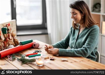 winter holidays, diy and hobby concept - woman making advent calendar or packing christmas gift at home. woman making advent calendar on christmas at home