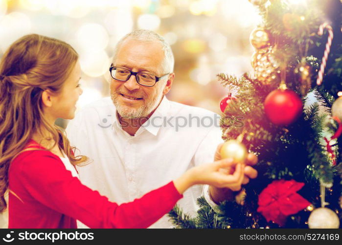 winter holidays, family and people concept - happy grandfather and granddaughter decorating christmas tree happy over lights background. grandfather and granddaughter at christmas tree