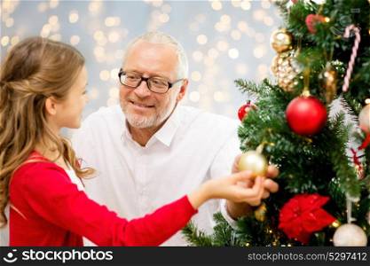 winter holidays, family and people concept - happy grandfather and granddaughter decorating christmas tree happy over lights background. grandfather and granddaughter at christmas tree