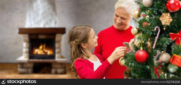 winter holidays, family and people concept - happy grandmother and granddaughter decorating christmas tree over home room with fireplace. grandmother and granddaughter at christmas tree