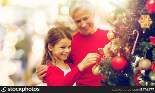 winter holidays, family and people concept - happy grandmother and granddaughter decorating christmas tree over lights background. grandmother and granddaughter at christmas tree
