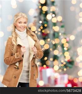 winter holidays, fashion and people concept - smiling young woman in winter clothes over christmas tree lights background