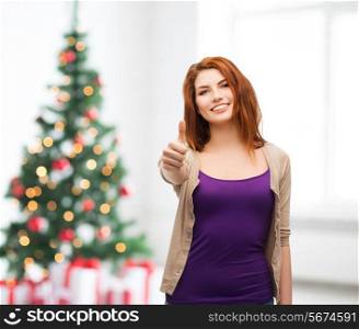 winter holidays, gesture and people concept - smiling teenage girl in casual clothes showing thumbs up over living room and christmas tree background