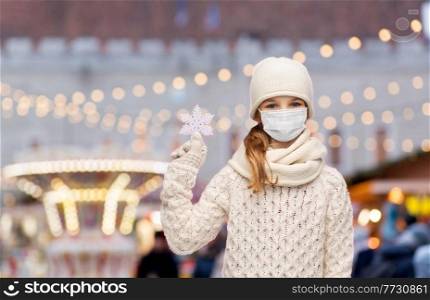 winter holidays, health and people concept - smiling girl in mask with snowflake decoration over christmas market or amusement park lights on background. girl in mask with snowflake over christmas market