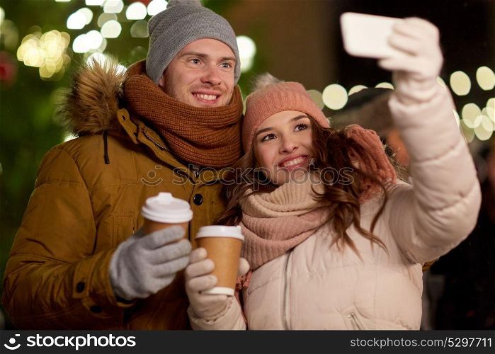 winter holidays, hot drinks and people concept - happy couple with coffee taking selfie in christmas evening. couple with coffee taking selfie at christmas