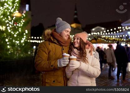 winter holidays, hot drinks and people concept - happy young couple with coffee at christmas market in evening. happy young couple with coffee at christmas market